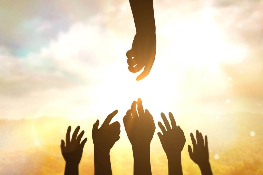 Group of hands reaching upwards towards sunlit sky with single hand reaching towards them